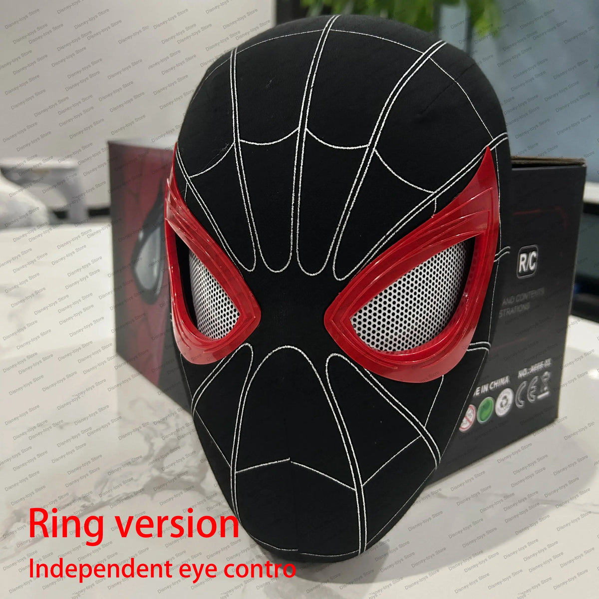 Spider mask with black base, white web pattern, red eye frames, and mesh eye openings, displayed on a table.
